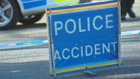 A blue Police Accident sign, with part of a police car in the background.