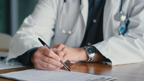 Man in white coat holding pen with a clipboard