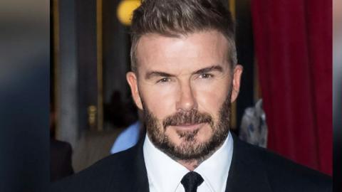 David Beckham wearing a white shirt with black tie and black suit blazer