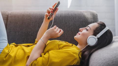 A woman listening to music using headphone (stock image)