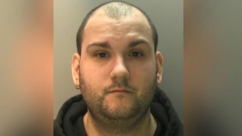 A balding man, with one earring, wearing a black hoodie.