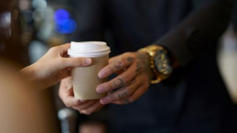 A barista hands a customer a takeaway coffee