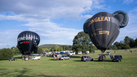 Two hot air balloons tethered at Longleat safari park. They are both black. One says 'Longleat' on it, while the other advertises Wednesday on Netflix. 