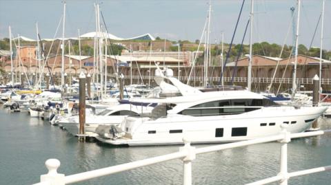 Yachts at the St Helier harbour, with Fort Regent in the background and white iron railings in the foreground.