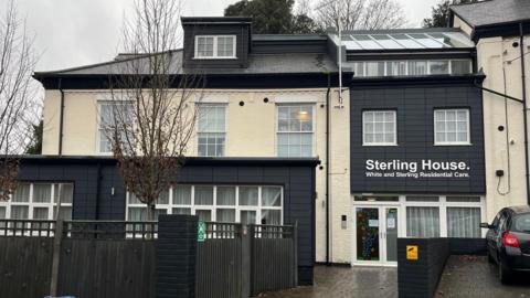 The outside of Sterling House in Norwich. The building is painted cream with some sections including the room painted black. There is a sign on the building which says Sterling House, on it. 