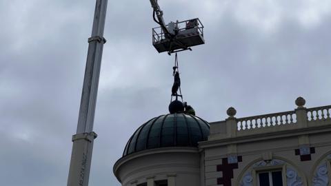 A crane lifting the statue of Roman messenger god Mercury on top of the Lyceum Theatre dome