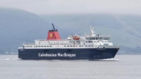 The MV Caledonian Isles is a ship with a black lower section with the words Caledonian MacBrayne printed in white along the side of the ship. In smaller white text near the front reads the words Caledonian Isles. The ship is white from the deck up. It sails along the water on a cloudy day. 