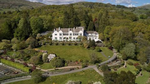 An aerial view of Brockhole-on-Windermere. A large white building is surrounded by gardens and trees.