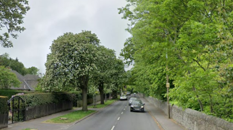 A stretch of road in a suburban area with a wall and houses on one side and a wall on the other