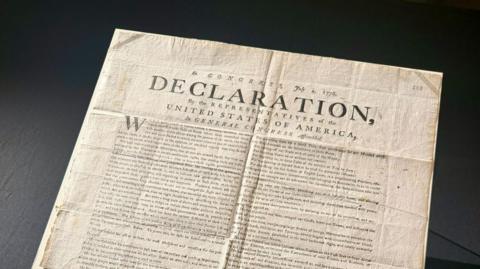 A copy of the US Declaration of Independence. The word "declaration" can be seen in capital letters on the document, which has various folds and creases.