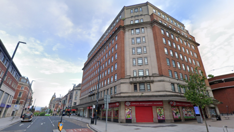 A ten story building with red and beige brick next to a road with traffic lights.