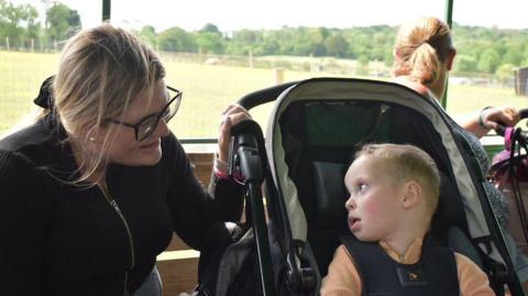 A woman looks lovingly at her baby son. He is in a push chair.