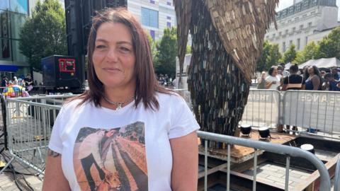 Roseann Taylor standing in front of the Knife Angel wearing a white t-shirt with a picture of her son on it