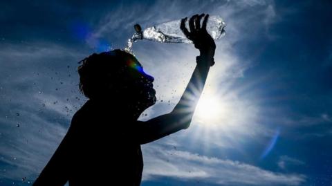 A photo of a person pouring water over their head with bright sunshine in the background