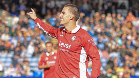 Anis Mehmeti holds his right arm out and points his finger and smiles