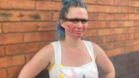 A woman with a line of black face paint covering her eyes and a red hand mark over her mouth