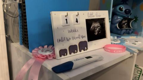 A table with a pregnancy test and a board saying "14 weeks until we meet you" and a picture of an ultrasound.