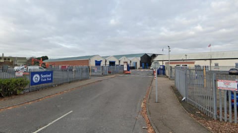 The entrance to a business park with a blue and white sign reading "sentinel trade park". it has silver metal gates and a barrier for vehicles