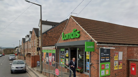 An exterior shot of a village post office and supermarket with a man exiting