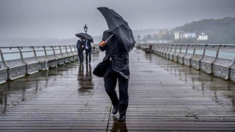 A man hold an umbrella in strong rains and winds on a wooden pier