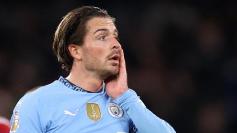 Jack Grealish in Manchester City kit with his left hand raised to his face