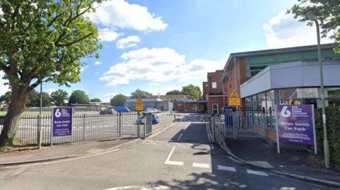 A picture of the car park entrance to The Sixth Form College in Farnborough. A few cars are parked there. It's sunny day.