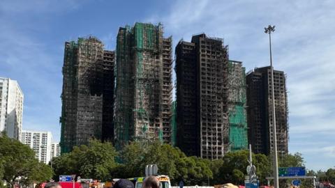 Large building complex from afar - burnt and hollowed out with green mesh and scaffolding visible.
