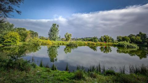 The edge of a weather front moves over a lake surrounded by trees