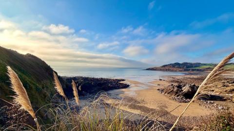 Blue sky with some clouds over a sea inlet with rugged land around 