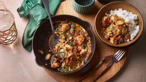 Top down view of a brown dish with chicken in a sauce with a spoon in it