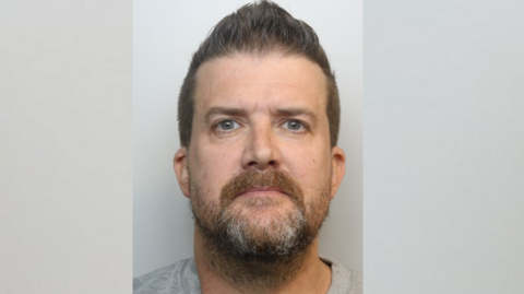 Man with beard and brown hair in a mugshot