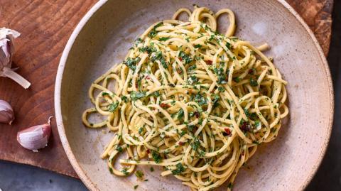 A bowl of spaghetti with chilli flakes and herbs on a wooden board 
