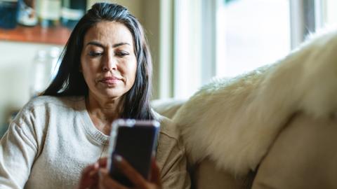 Woman using smartphone on sofa in front of window at home