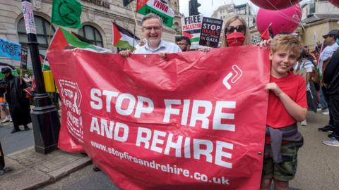 Protesters carry a banner saying "stop fire and rehire"