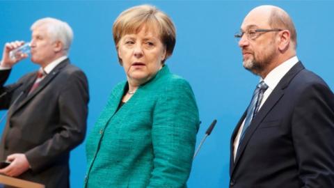 German Chancellor Angela Merkel, Christian Social Union (CSU) leader Horst Seehofer and Social Democratic Party (SPD) leader Martin Schulz stand on stage in an off-guard shot