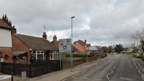 Google Streetview of 75-79 New Road, Peterborough. There are houses on the left side of the road and a roundabout in the distance.