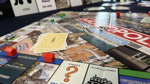 A Monopoly board game with houses and player pieces on the board which features locations like Chichester Cathedral