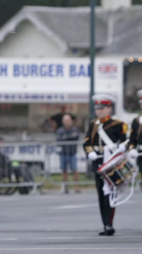 Drummers in a military band walking along a concrete path in full uniform.