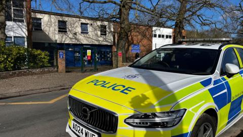 A police car parked in front of the two-storey school building.