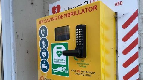 A yellow safe containing a defibrillator.