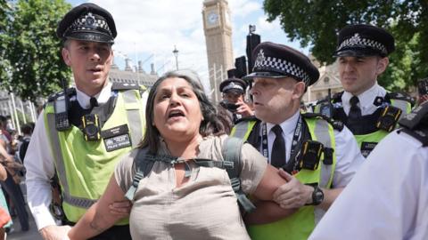 A woman is led away by police officers as supporters of Palestine Action take part in a mass action in Parliament Square