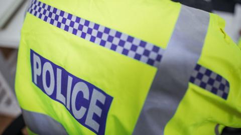A close-up of the back of a police officer's high-visibility jacket. It reads 'Police' on it.