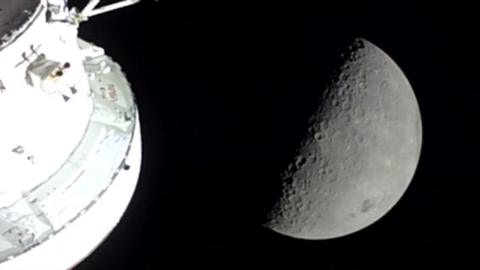 The moon is half covered in shadow, showing off its craters, with the capsule in the left of the photo