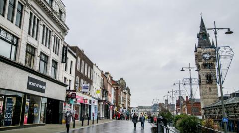 Darlington high street. A House of Fraser store is among a number of shops on the left side of the street. A clock tower stands on the right.