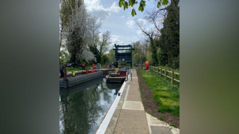 Work being carried out on a lock. A team of people are dotted around the canal on a clear day.