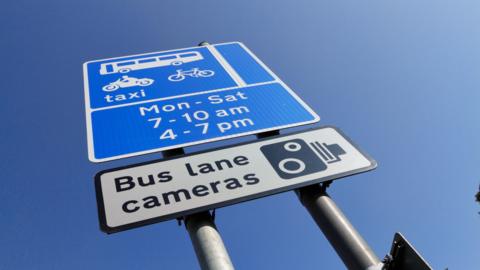 This is a typical sign alongside a bus lane in England. From the top, it describes: 1. Permitted traffic – buses, taxis, motorbikes and bicycles. 2. Times during which the bus lane is in operation – from Monday to Saturday at rush-hour times. 3. Warning sign that bus lane cameras are in operation. These cameras can be used as evidence of violations.