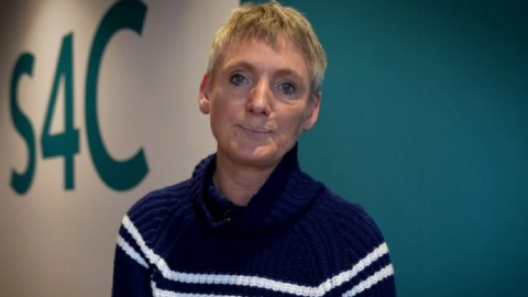 Sian Doyle looking at the camera. S4C is written on the wall behind.  