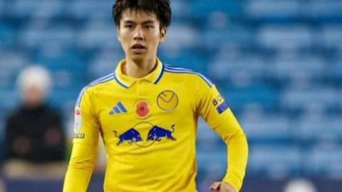 Ao Tanaka wearing the yellow Leeds United shirt to be auctioned during Leeds' match against Millwall on 6 November