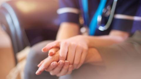 A nurse comforting a patient by holding their hand 