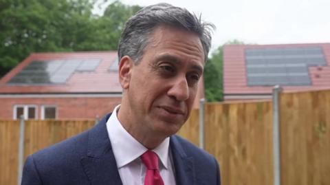 Ed Miliband standing in front of two houses with solar panels on the roofs